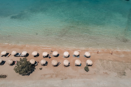 An aerial view of a beach with rows of thatched umbrellas and lounge chairs.