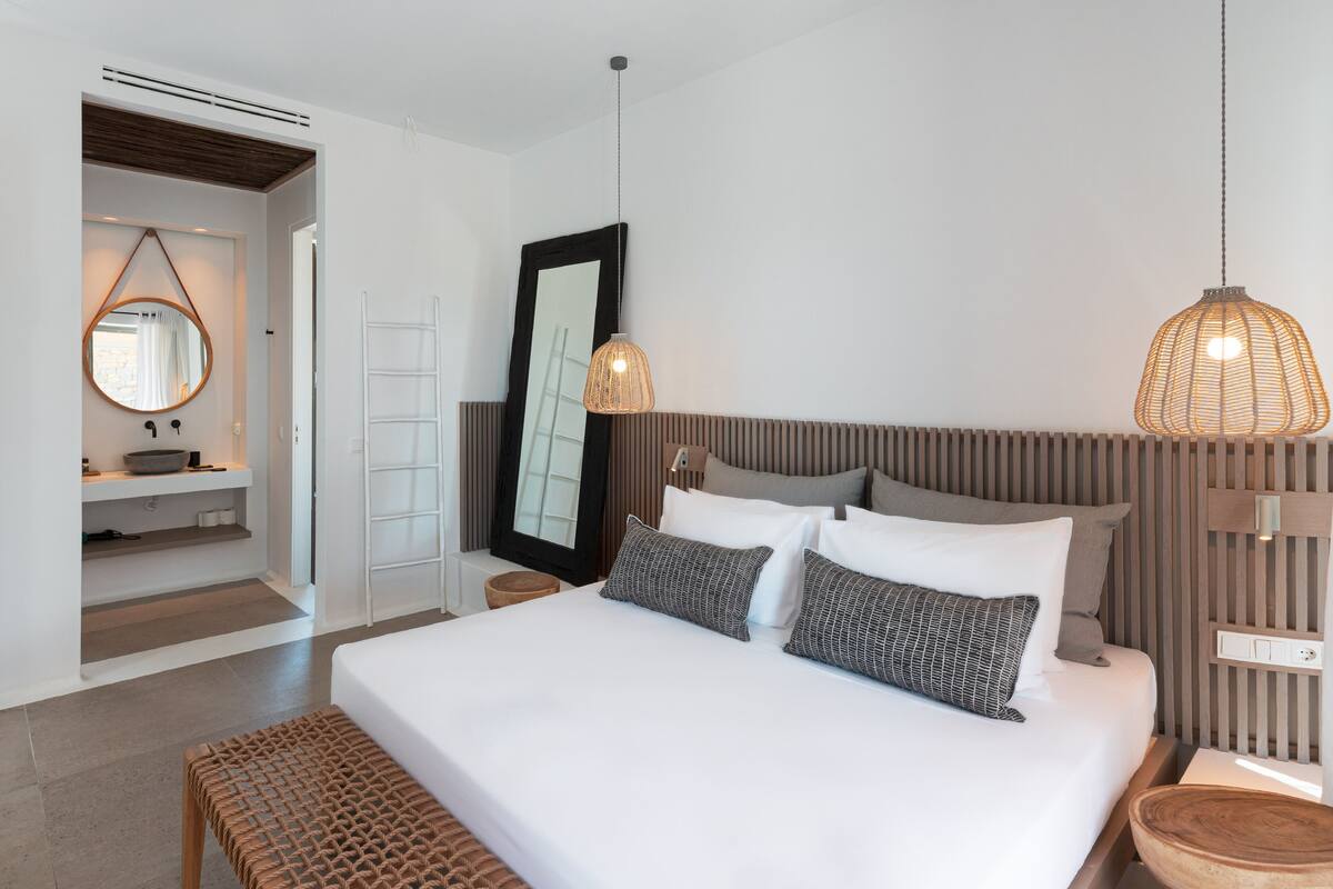 Un dormitorio moderno con una cama grande, mesitas de noche, un espejo y una lámpara colgante.