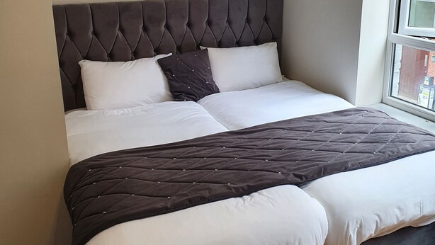 A modern bedroom with a tufted headboard, a large bed with white and dark grey bedding, and a wooden floor. - City Centre, Detached 10 Person Accommodation (Liverpool)