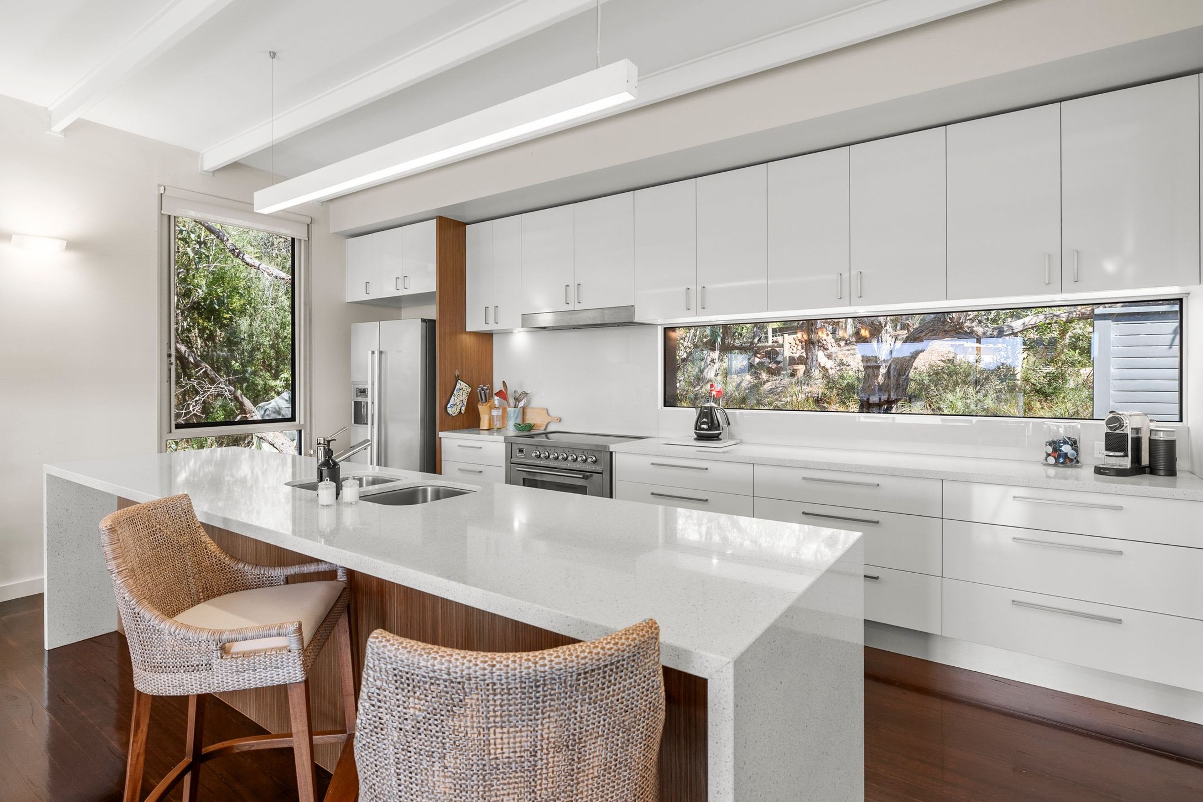 A modern kitchen with white cabinetry, a large island with bar stools, and a view of a natural landscape through the windows.