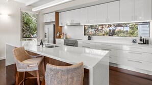 A modern kitchen with white cabinetry, a large island with bar stools, and a view of a natural landscape through the windows.