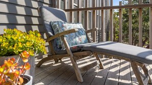 A wooden deck with a single lounge chair featuring a cushion and a pillow.
