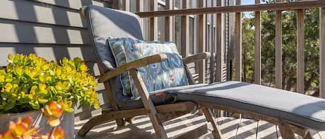 Una terraza de madera con una única silla de descanso con cojín y almohada.