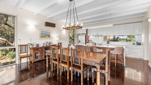 A spacious dining area with a wooden table and chairs, a hanging light fixture, and a view of the outdoors through large windows.