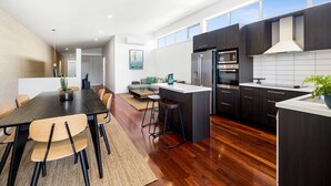 Une cuisine moderne avec des meubles de couleur sombre, un îlot central et un coin repas comprenant une table et des chaises en bois.