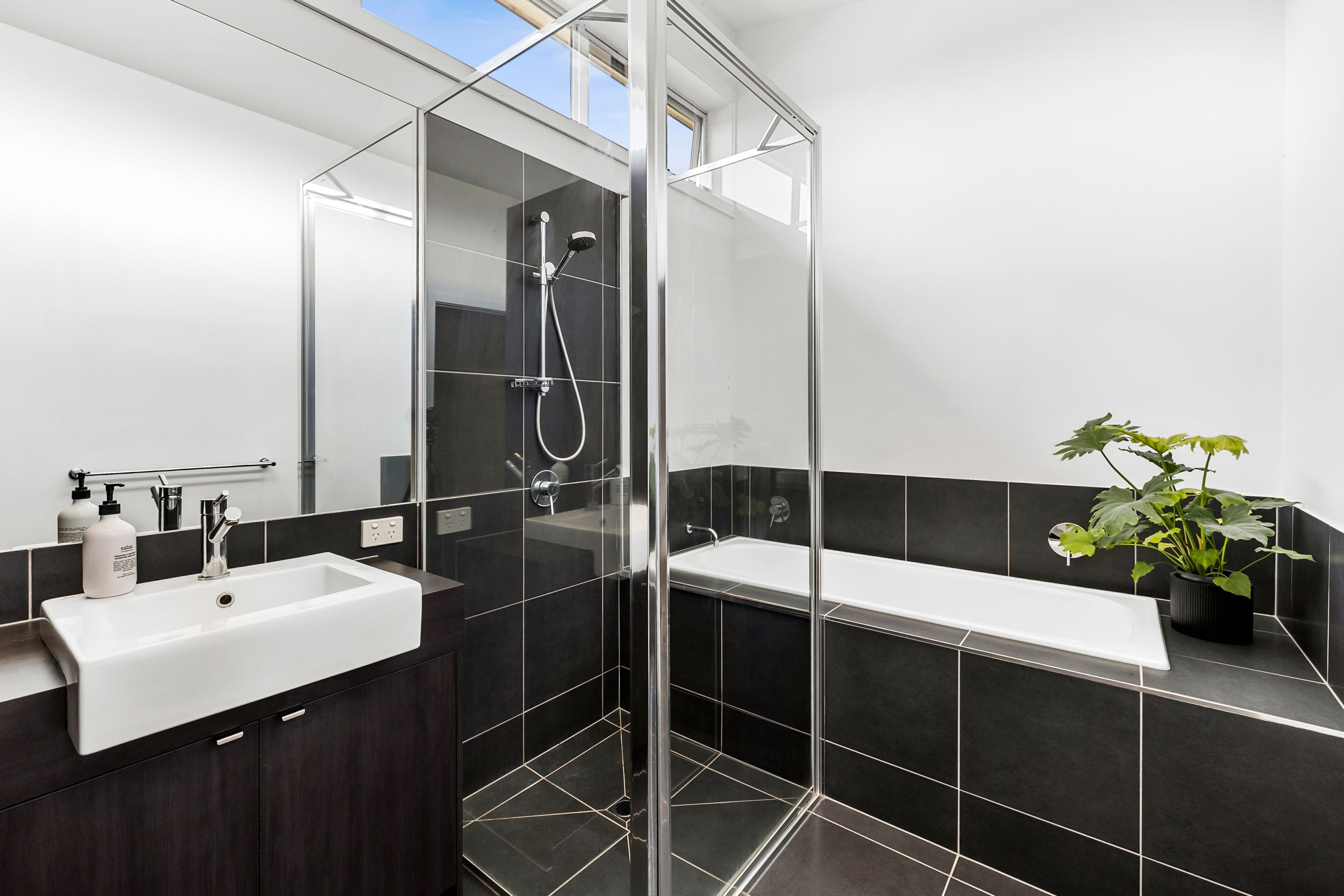 A modern bathroom with a glass shower enclosure, a white sink, and a potted plant.