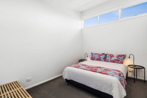 A bedroom with a bed, a nightstand, a lamp, and a window. - Beach Baby (Aireys Inlet)