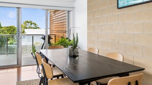 A modern dining area with a dark wooden table, beige chairs, and a glass-top table with a potted plant.