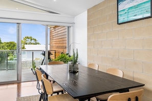 A modern dining area with a dark wooden table, beige chairs, and a glass-top table with a potted plant.