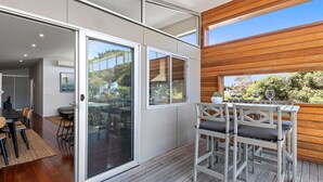 Un espace de restauration extérieur moderne, doté d’une terrasse en bois, d’une porte vitrée donnant sur un espace intérieur et offrant une vue sur l’extérieur.