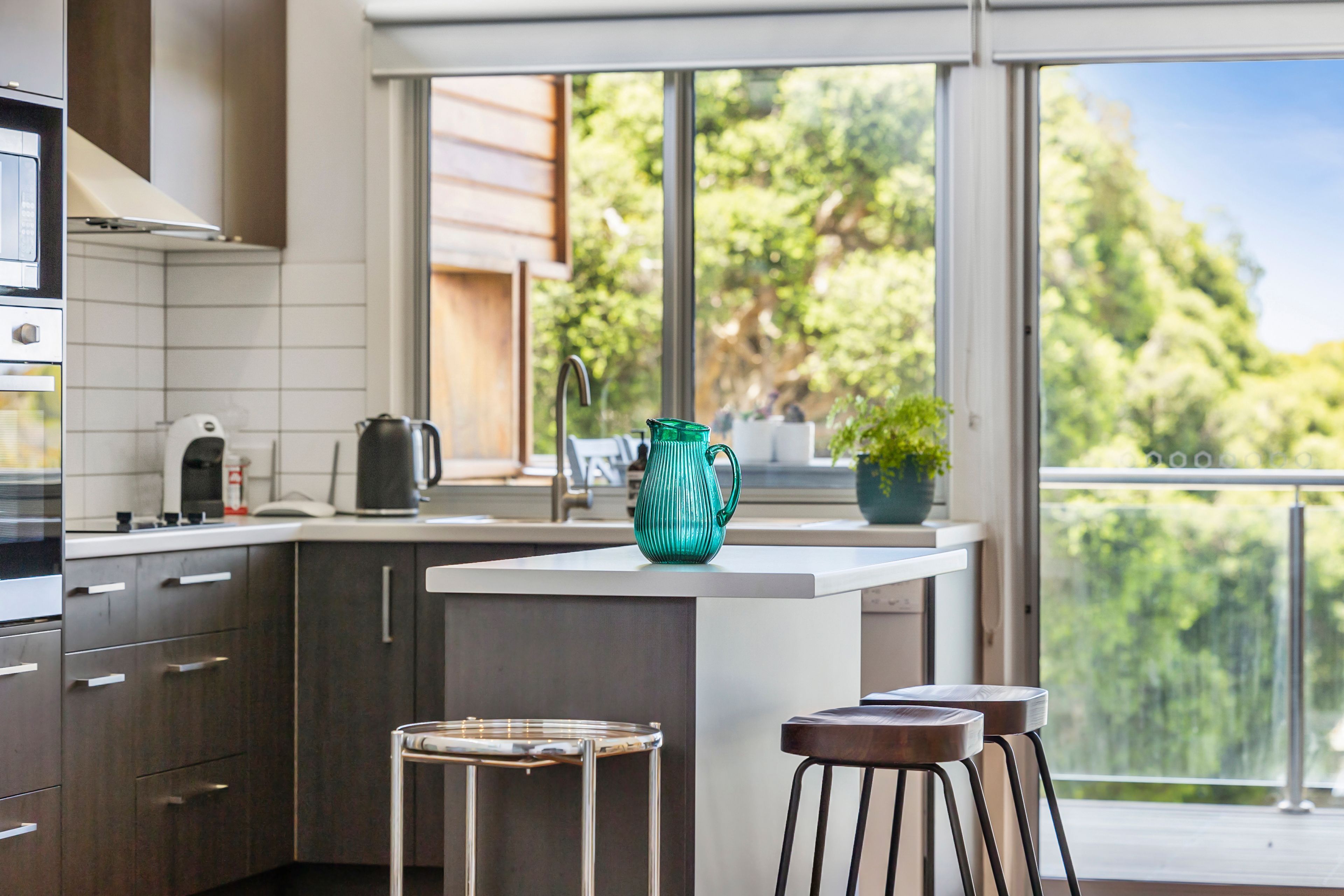 Una cocina moderna con una isla central, electrodomésticos de acero inoxidable y vistas a la vegetación a través de grandes ventanales.