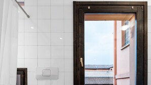 Un baño con inodoro, bidé y ventana con vistas a edificios.