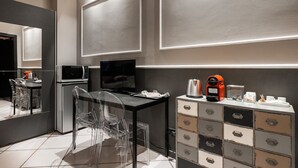 Una cocina moderna con microondas, refrigerador y cafetera. Hay una mesa de vidrio con sillas y un televisor sobre un mueble.