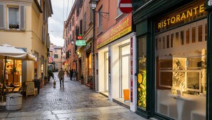 Una calle empedrada bordeada de tiendas, entre ellas un restaurante y una pizzería.