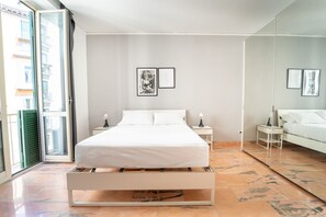 Un dormitorio moderno con cama, dos mesitas de noche, una mesita auxiliar, un espejo grande y una puerta corredera a la izquierda.