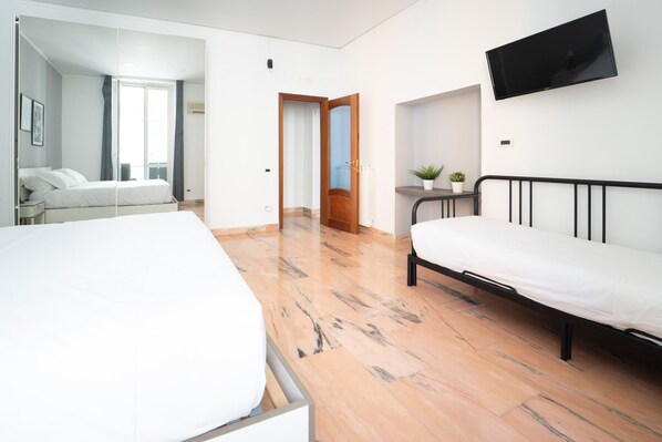 A hotel room with two beds, a TV, a small table with a plant, and a door leading to another room.