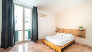 A bedroom with a bed, a window with curtains, a plant, and a wooden headboard.