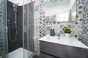 Un baño con ducha, lavamanos con artículos de aseo y espejo.