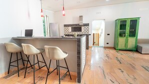 A modern kitchen with a bar area, three bar stools, a green cabinet, and a grey sofa.