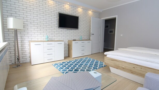 Un dormitorio moderno con pared de ladrillo blanco, televisor de pantalla plana, cama con cabecera de madera y una mesa de centro de vidrio.