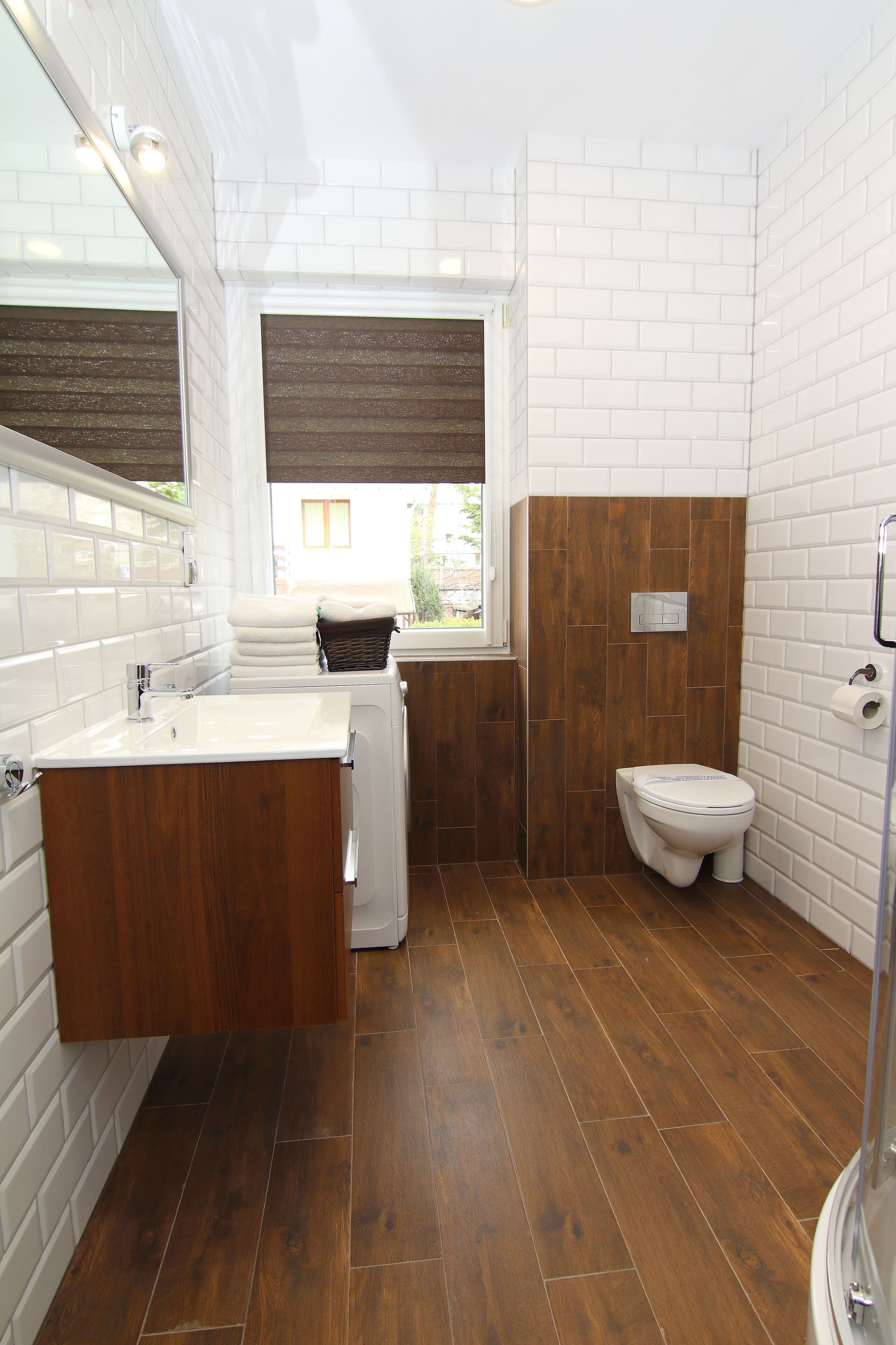 A bathroom with a white sink, wooden vanity, a white toilet, and a shower area.