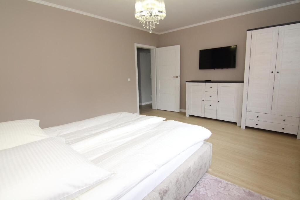 A bedroom with a large bed, a wardrobe, a television, and a chandelier.