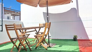 En terrasse med et bord, stole, en beige parasol og en lille potteplante.