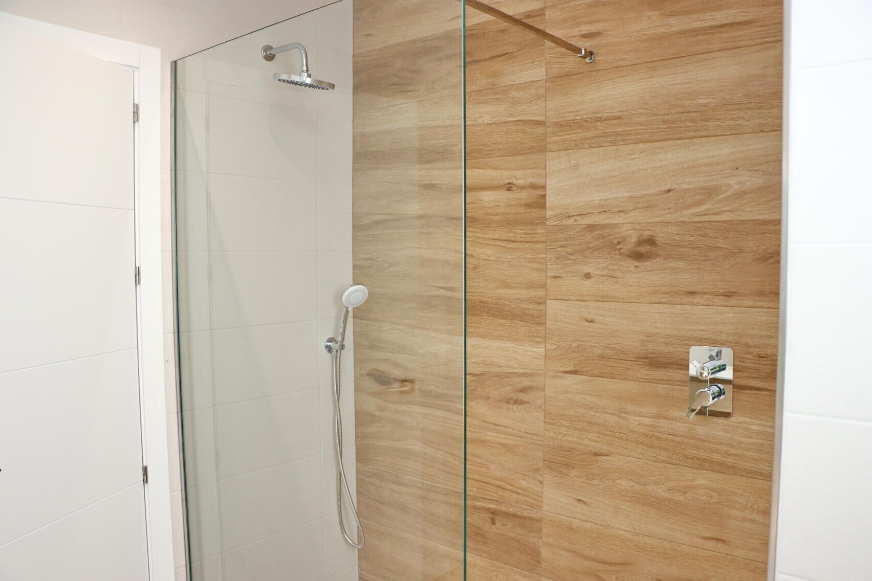 A modern bathroom with a glass shower enclosure, a wooden panel wall, and a white door.