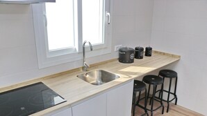 Et køkken med en stålvask, en sort induktionskogetop og tre sorte barstole.
