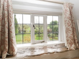 Quarto com uma janela grande, moldura branca e vista para um jardim.