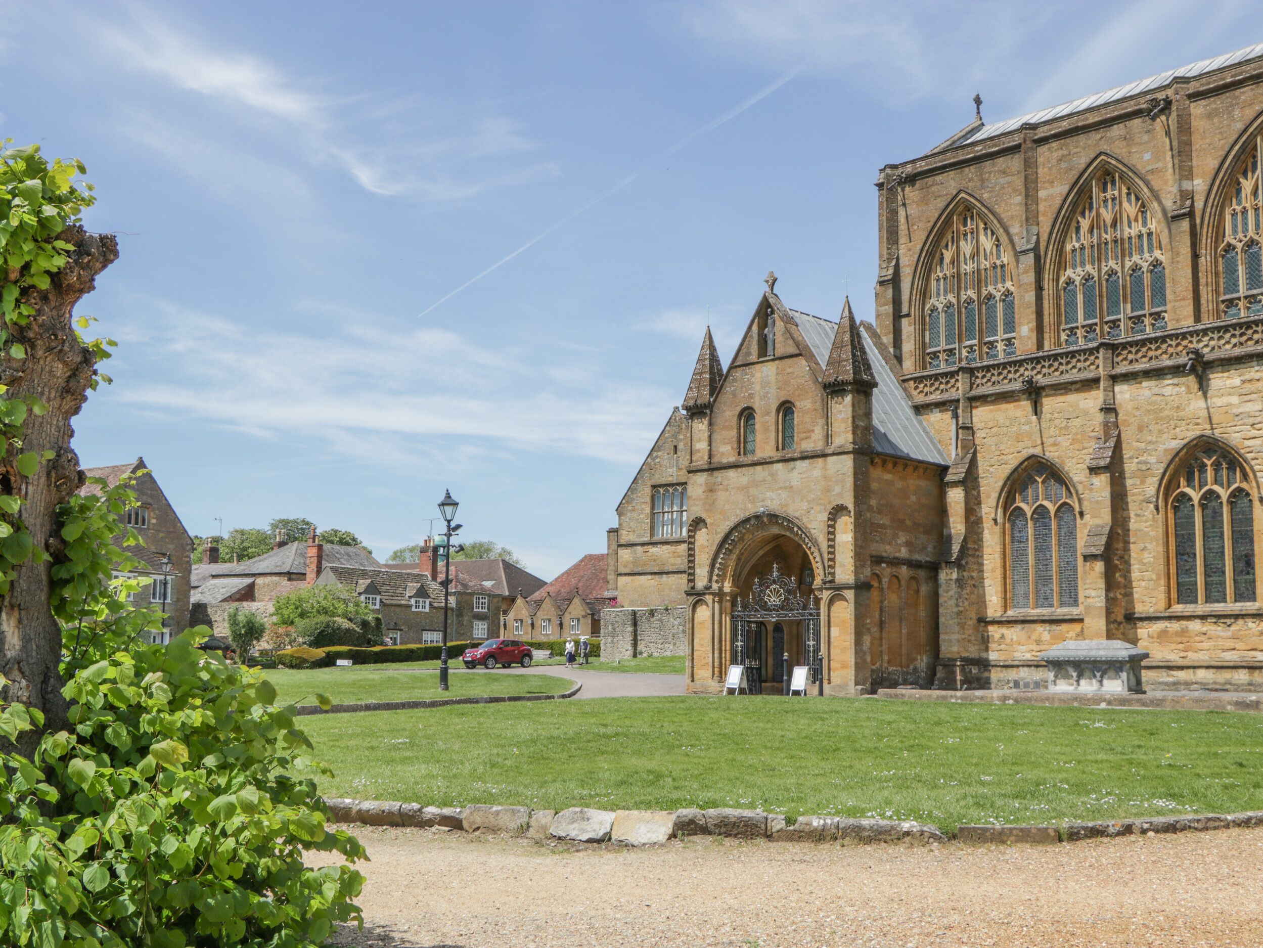 A historic building with a large arched entrance, a stone facade, and a well-maintained lawn in front.