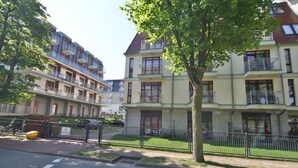 A residential building with multiple balconies, a paved driveway, and a tree in the foreground. - Apartamenty Swinoujscie - Roza Wiatrow (Swinoujscie)
