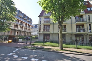 A residential building with multiple balconies, a paved driveway, and a tree in the foreground.