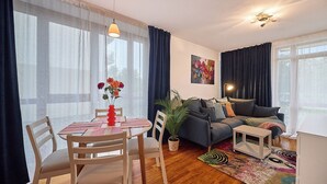 A living room with a sofa, a dining table with chairs, a potted plant, and a painting on the wall. - Apartamenty Swinoujscie - Roza Wiatrow (Swinoujscie)