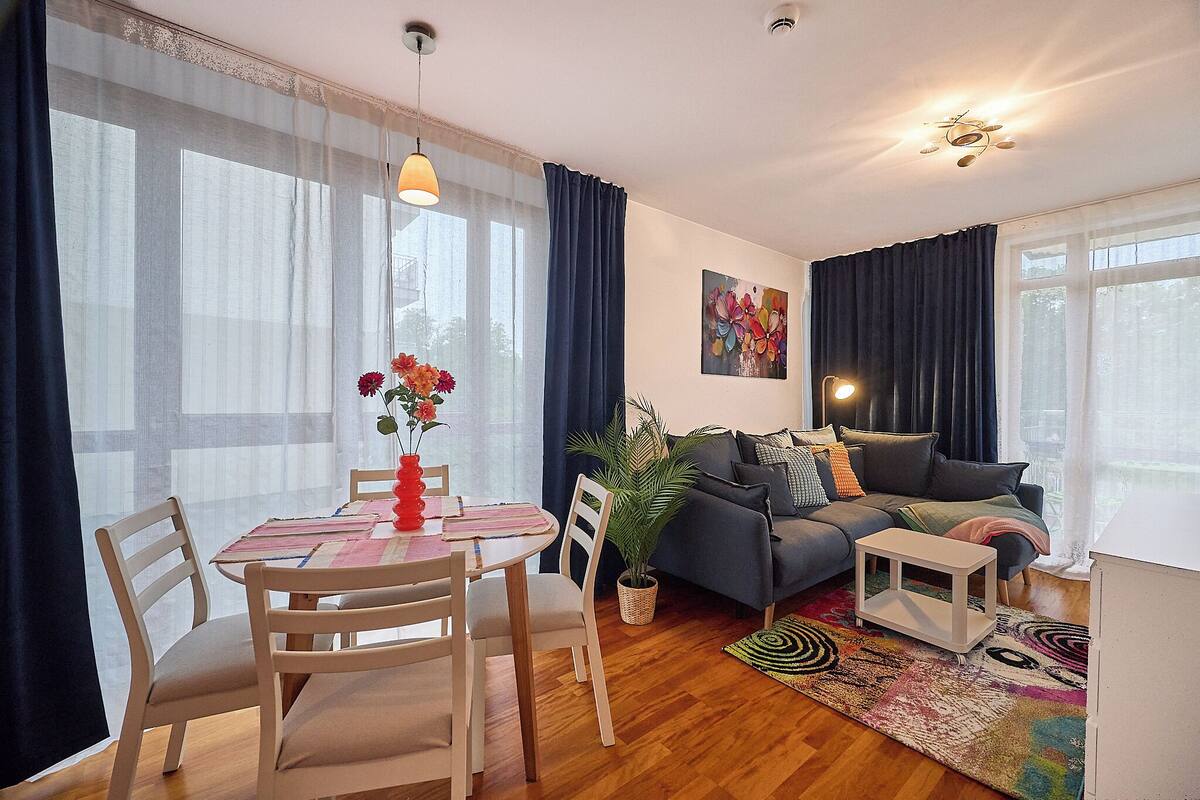 Una sala de estar con sofá, una mesa de comedor con sillas, una planta en maceta y un cuadro en la pared.