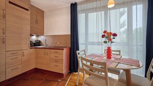 A modern kitchen with wooden cabinets, a dining table with chairs, and a vase of flowers. - Apartamenty Swinoujscie - Roza Wiatrow (Swinoujscie)
