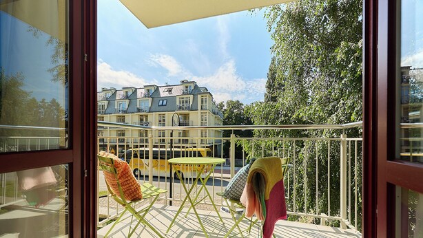A balcony with a yellow chair, a green folding chair, and a table with a blanket. - Apartamenty Swinoujscie - Roza Wiatrow (Swinoujscie)