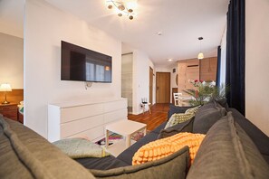 A modern living room with a flat-screen TV, a sofa, a small coffee table, and a dining area in the background. - Apartamenty Swinoujscie - Roza Wiatrow (Swinoujscie)