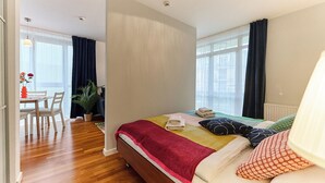 A hotel room with a bed, a dining area with chairs, a table, and a potted plant. - Apartamenty Swinoujscie - Roza Wiatrow (Swinoujscie)