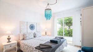 Een slaapkamer met een bed, nachtkastjes, een kroonluchter en uitzicht op groen buiten.