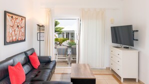Een woonkamer met een zwarte leren bank, rode kussens, een houten salontafel, een witte tv-meubel en een schilderij aan de muur.