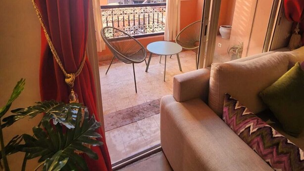 A balcony with a sofa and chairs, a potted plant, and a view of buildings. - Appartement PATIO GUELIZ (Marrakech)