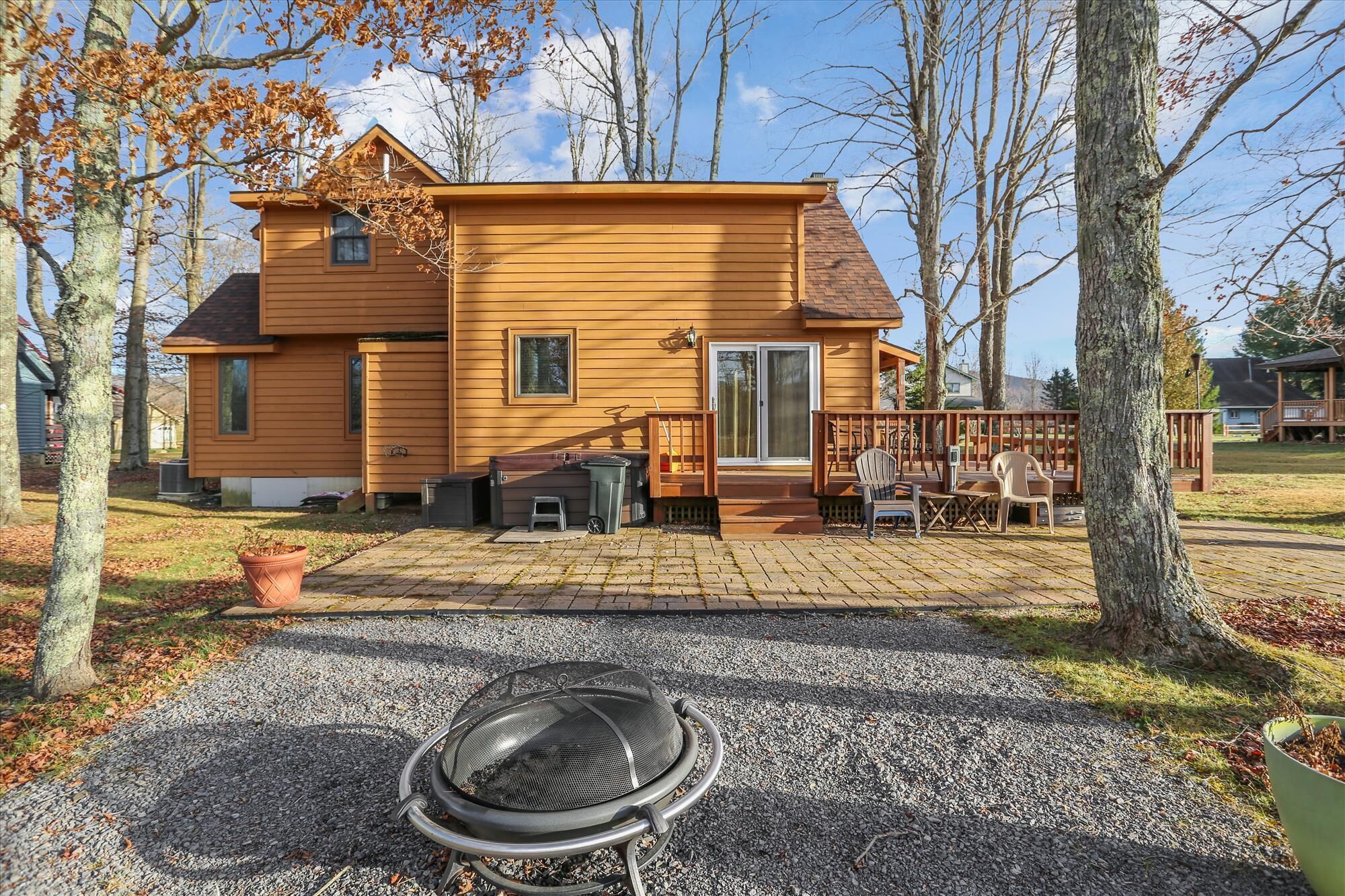 A two-story wooden house with a deck and a fire pit in the front yard.
