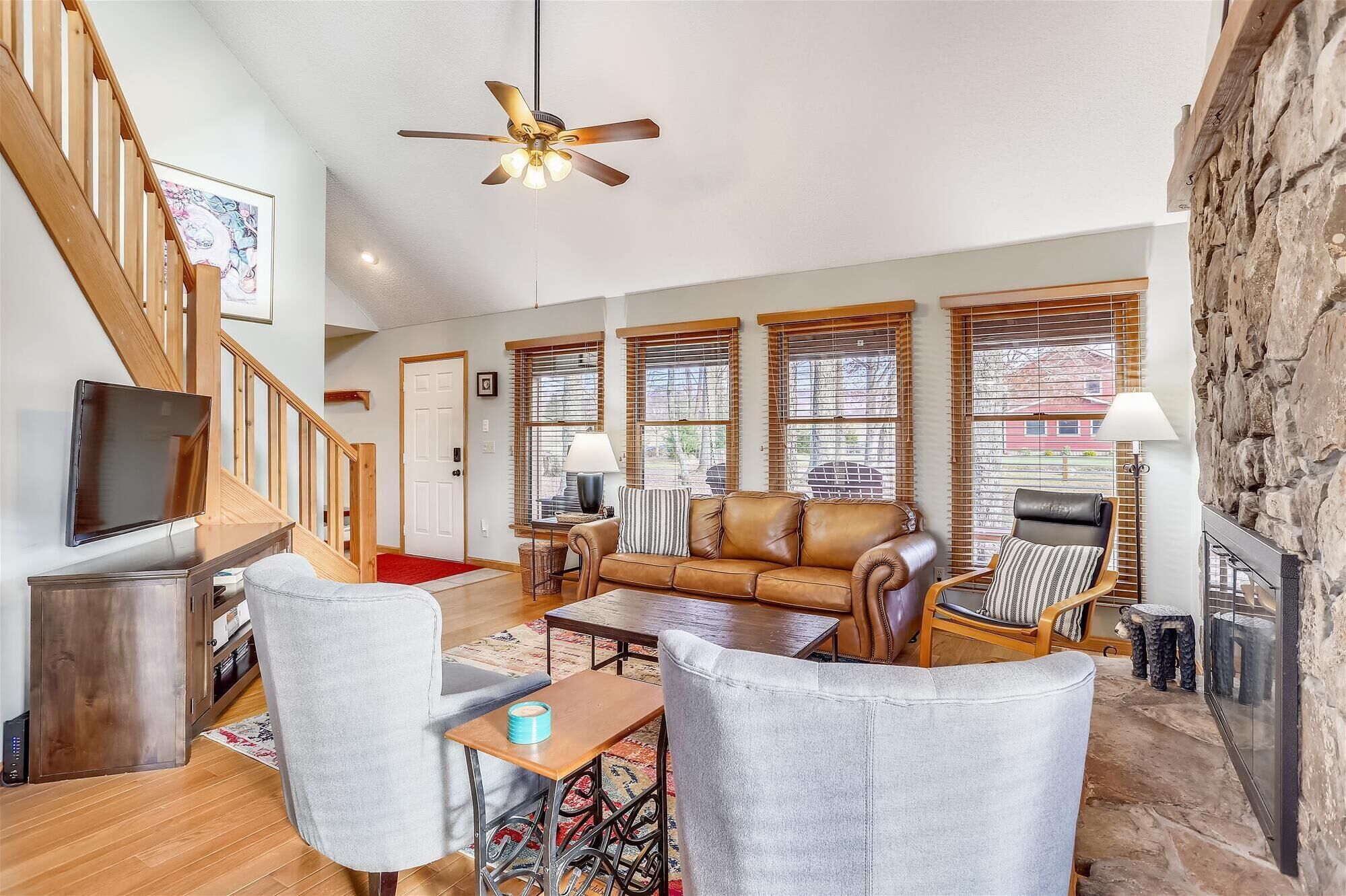 A spacious living room with a wooden staircase, a leather sofa, a TV, and a stone wall.