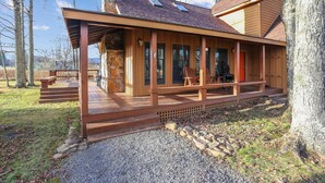 Una cabaña con terraza de madera, paredes de piedra y un porche cubierto con sillas.