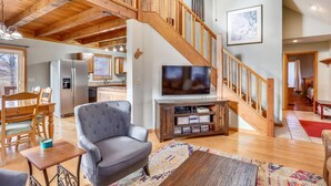 Amplia sala de estar con escalera de madera, televisor y comedor con mobiliario de madera.