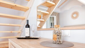A wooden table with a bottle of wine, two wine glasses, and a decorative jar with stones. - Korina Apart Hotel (Corfu)