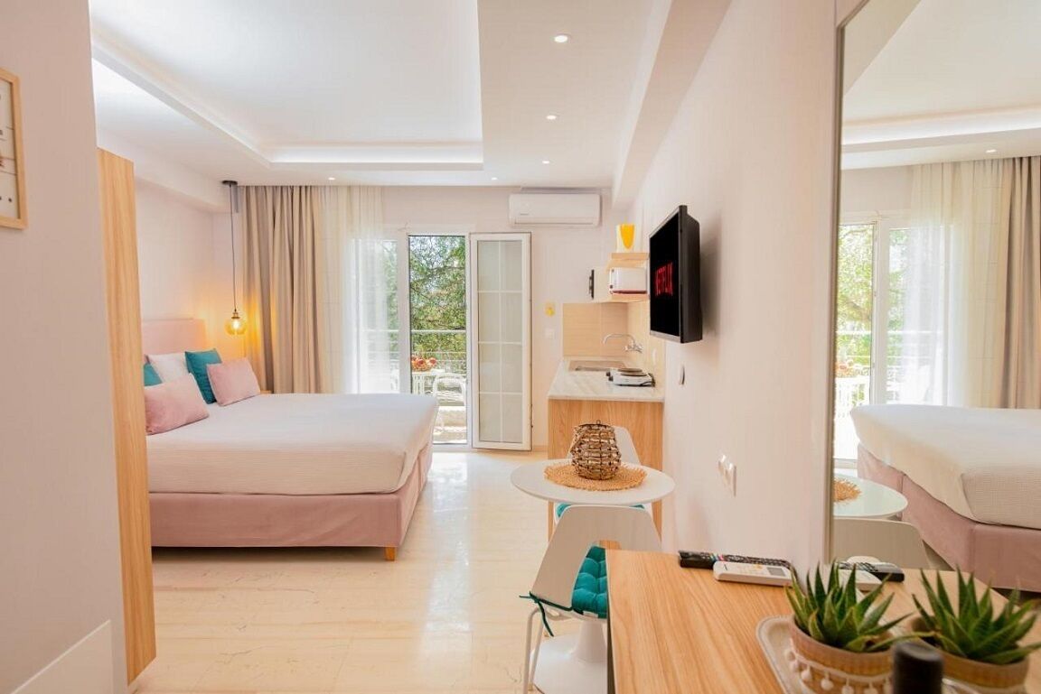 Quarto de hotel com uma cama, uma pequena mesa de escritório, televisão e varanda com cortinas.