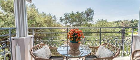 Een balkon met rieten stoelen, een glazen tafel en een bloempot met rode bloemen.