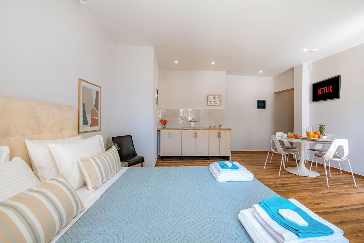 A hotel room with a bed, a desk, a kitchenette, and a TV.